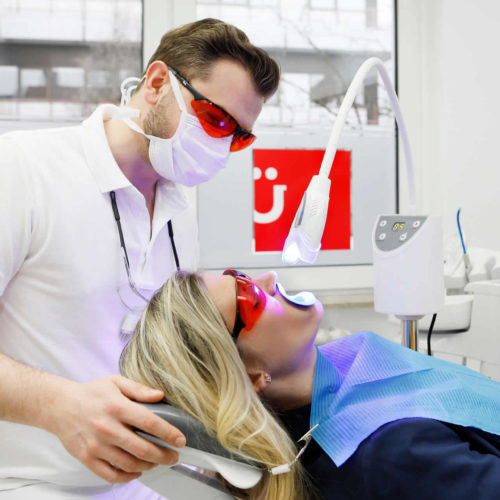 bleaching behandlung frau auf zahnarztstuhl rote schutzbrille