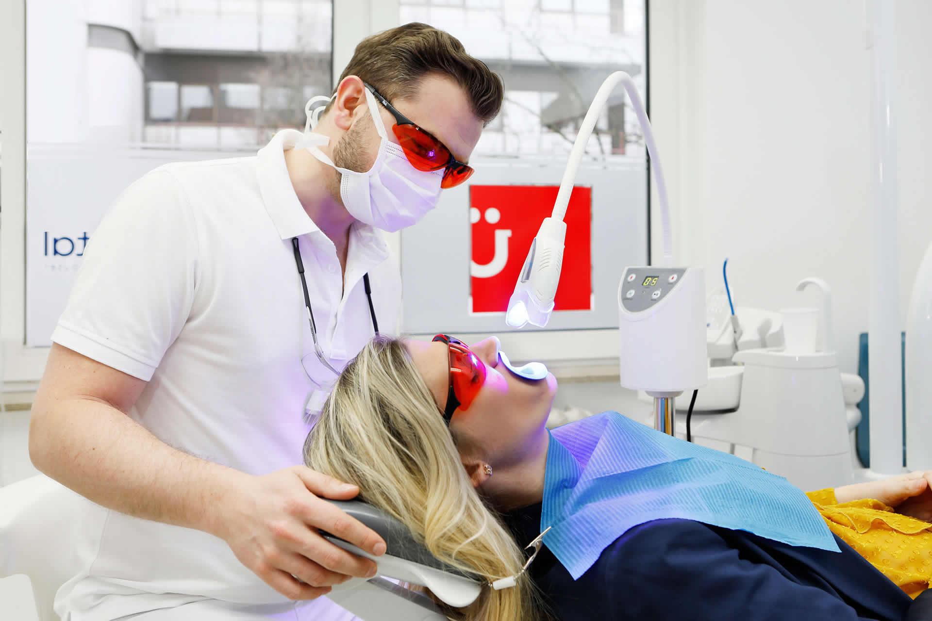 bleaching behandlung frau auf zahnarztstuhl rote schutzbrille